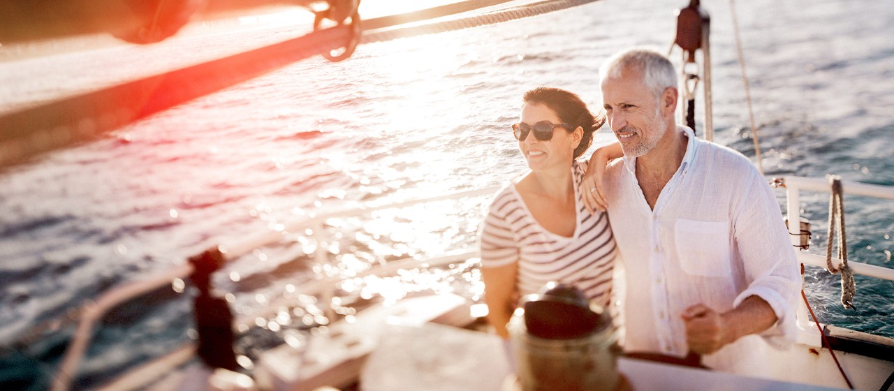 Ehepaar steht am Steuer eines Segelschiffs und hält sich im Arm